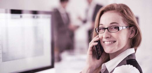 Kontakt: Service-Mitarbeiterin mit Telefon vor einem Bildschirm